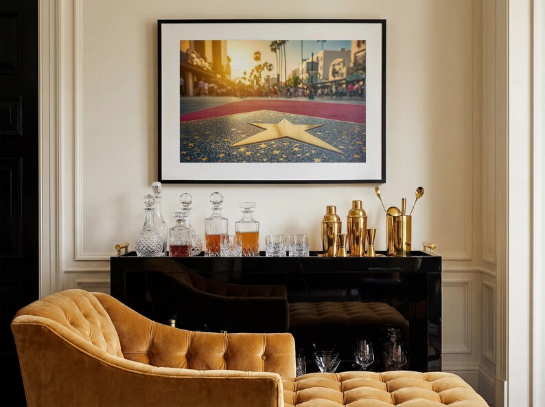 May include: A framed photograph of the Hollywood Walk of Fame with a gold star. Below the photograph is a black bar cart with decanters, glassware, and gold bar tools. A gold chaise lounge is in the foreground.