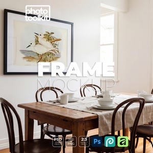 May include: A black rectangular frame containing a print of two white birds perched in a nest, mounted on a white wall above a wooden dining table with chairs, featuring the text "FRAME MOCKUP" overlaid in large white letters across the center.