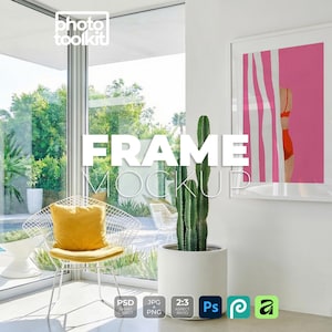 May include: A white rectangular picture frame hanging on a wall, containing a print of a person in a red swimsuit standing behind white and pink vertical stripes. The frame is positioned next to a tall green cactus in a white cylindrical planter.