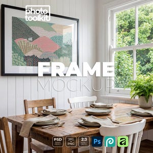 May include: A black rectangular picture frame containing an abstract landscape print with green, pink, and beige patterns, mounted on a white paneled wall above a wooden dining table set with plates, napkins, and a small green potted plant.