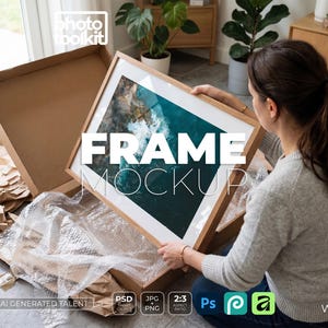 May include: A rectangular wooden picture frame containing an aerial photograph of a rocky coastline with turquoise ocean waves. The frame is being removed from a cardboard shipping box filled with protective bubble wrap and brown paper packing.