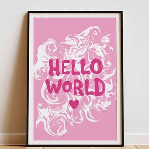 Könnte beinhalten: Ein gerahmter rosa Kunstdruck mit den Worten "HELLO WORLD" in einer Blasen-Schriftart, mit einem weißen Wirbeldesign und einem kleinen Herzen. Der Druck wird auf einem Holzboden vor einer weißen Wand ausgestellt.
