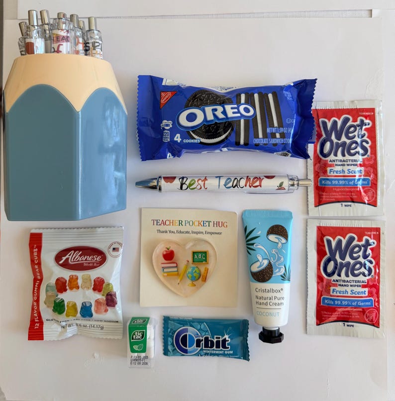 Peut inclure: Un porte-crayons bleu et cr&egrave;me contenant des stylos, un paquet de biscuits Oreo, deux sachets de lingettes antibact&eacute;riennes Wet Ones, un stylo Best Teacher, un jeton en forme de c&oelig;ur Teacher Pocket Hug, un tube de cr&egrave;me pour les mains Cristalbox &agrave; la noix de coco, un paquet d'oursons en g&eacute;latine Albanese, une petite bo&icirc;te de Tic Tac et un paquet de chewing-gum Orbit &agrave; la menthe.