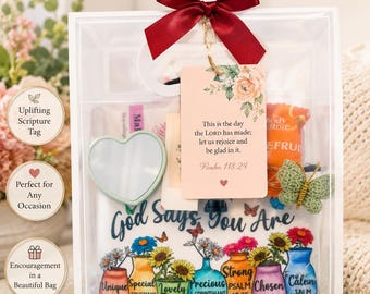 Puede incluir: Una bolsa de regalo transparente con un lazo burdeos, que contiene una etiqueta de escritura, un espejo en forma de corazón y otros artículos. La bolsa presenta el texto "Dios dice que eres" con jarrones y flores coloridas. La bolsa está etiquetada como "Christian Gift Bag".