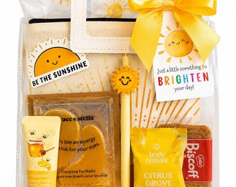 Puede incluir: Una cesta de regalo con un exterior de plástico transparente, que presenta una variedad de artículos con temática amarilla. Incluye una crema de manos, mascarillas para los ojos, vaporizadores de ducha, una vela y una galleta. La bolsa tiene un asa y un lazo amarillo.