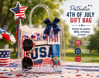 Puede incluir: Una bolsa de regalo de plástico transparente que contiene una camiseta blanca con el texto USA, gafas de sol rojas, blancas y azules, y un sobre de bebida Liquid I.V. La bolsa tiene un lazo azul marino, una etiqueta Happy 4th of July y un adorno.