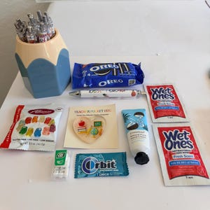 Peut inclure: Un porte-stylo en forme de crayon contenant des stylos, un paquet de biscuits Oreo, un stylo marqu&eacute; Best Teacher, deux paquets de lingettes antibact&eacute;riennes Wet Ones, un sachet d'oursons en g&eacute;latine Albanese, une carte en c&oelig;ur, de la cr&egrave;me pour les mains.