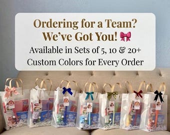 Puede incluir: Siete bolsas de regalo transparentes con asas, cada una con artículos variados y rematada con un lazo de color. Un cartel blanco arriba dice: Ordering for a Team? We've Got You! Available in Sets of 5, 10 & 20+ Custom Colors for Every Order.
