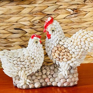 Figura vintage de gallo y gallina cubiertos de conchas marinas con ojos saltones.
