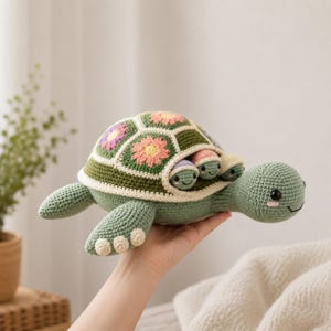 May include: A crocheted turtle toy featuring a shell constructed from green, pink, and purple floral granny squares. The large turtle has a light green body with dark eyes and three smaller baby turtles tucked into the side of its shell.