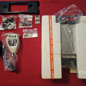 May include: A collection of vintage CB radio components, including a black faceplate, microphone, and various hardware pieces. The components are packaged in clear plastic bags and styrofoam. The text "DON'T FORGET TO ADJUST THE ANTENNA TRIMMER!!" is visible.