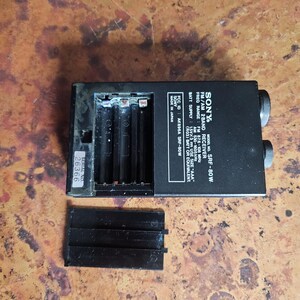 Puede incluir: Receptor de 2 bandas FM/AM Sony SRF-80W negro con compartimento de bater&iacute;a y tapa desmontada. La radio tiene dos perillas de sintonizaci&oacute;n y un n&uacute;mero de serie 26366. La radio est&aacute; fabricada en Jap&oacute;n.