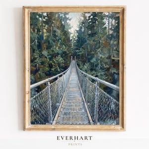 May include: A framed art print featuring a painting of a narrow suspension bridge with metal mesh railings leading into a dense forest of tall green and brown trees. The scene is captured from a centered perspective, showing the bridge path.