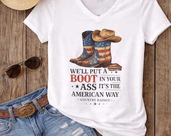 May include: White V-neck t-shirt with a graphic of cowboy boots and a hat, featuring the American flag design. The text reads "We'll put a boot in your ass it's the American way." Denim shorts and a straw hat are also visible.
