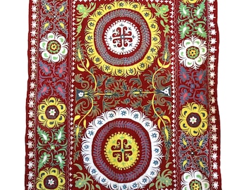 Könnte beinhalten: Ein rechteckiger, roter Textil mit aufwendiger Blumenstickerei. Das Design zeigt große, kreisförmige Medaillons in Gelb, Weiß und Blau, umgeben von detaillierten Blumenmustern in Grün und Gelb. Die Kanten sind mit einem dekorativen Rand versehen.
