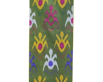May include: Green fabric with a repeating pattern of stylized floral and abstract shapes in yellow, pink, white, blue, and purple. The fabric has a woven texture and a vertical orientation.