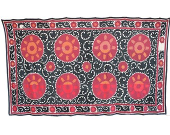May include: Rectangular textile with a black background featuring large, circular red and orange floral patterns. The border is red with small floral designs. The textile is likely a decorative piece, possibly a wall hanging or a rug.