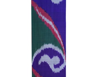 May include: A rectangular textile with a vibrant pattern. The design features large, stylized swirls in white against a deep purple background. Diagonal stripes in red and white accent the design, set against a green backdrop.