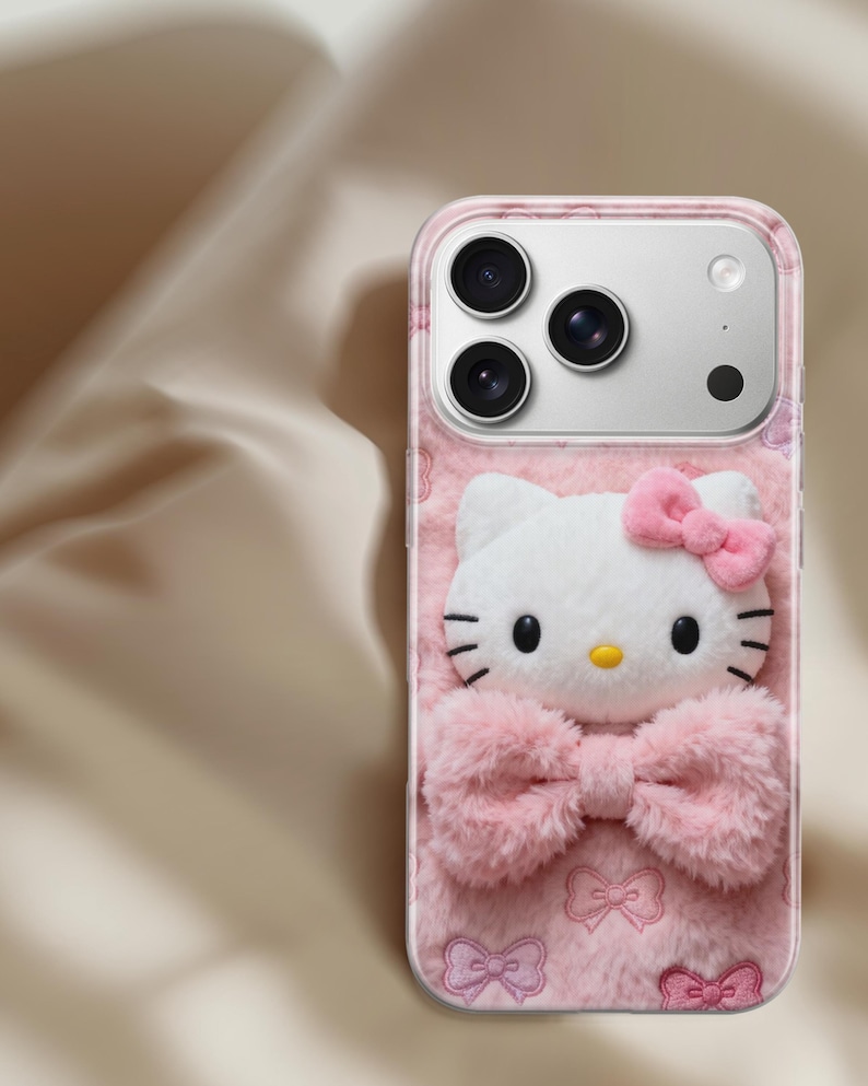Może przedstawiać: R&oacute;żowe etui na telefon z tr&oacute;jwymiarowym wzorem Hello Kitty. Etui ma puszystą fakturę z białą twarzą Hello Kitty, r&oacute;żową kokardą i r&oacute;żowym wzorem kokardek. Etui ma przezroczystą obw&oacute;dkę.