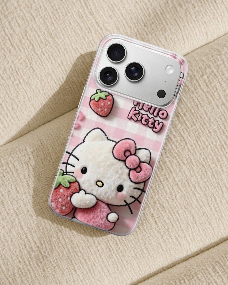 Może przedstawiać: Przezroczyste etui na telefon z motywem Hello Kitty w r&oacute;żowo-białą kratkę. Etui ma postać 3D Hello Kitty z r&oacute;żową kokardą i truskawkami. Na etui wydrukowano napis "hello kitty".