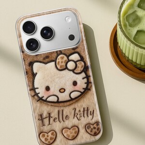 Może przedstawiać: Etui na telefon z motywem Hello Kitty. Etui ma brązową i beżową teksturę przypominającą futro z postacią Hello Kitty pośrodku. Słowa "Hello Kitty" są napisane pod postacią, wraz z trzema kształtami serca.