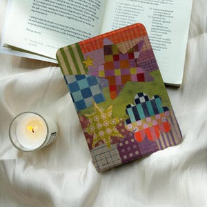 May include: A rectangular e-reader cover featuring a colorful patchwork design of stars, flowers, and geometric patterns in shades of green, orange, purple, and blue. The cover displays a vibrant, multi-textured aesthetic with various shapes.