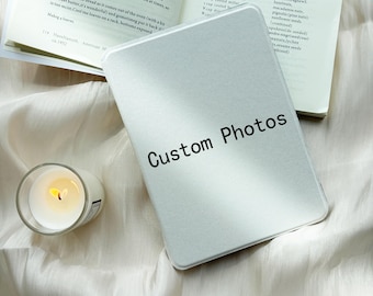 Può includere: Una scatola metallica rettangolare color argento con il testo Custom Photos stampato in nero sulla parte anteriore, posizionata accanto a un libro di cucina aperto e a un piccolo portacandele in vetro con una candela bianca accesa.