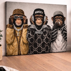 May include: A canvas print depicting three chimpanzees in designer attire. One wears a brown hat and sunglasses, another has headphones and a "GUCCI" sweater, and the third covers its mouth. The artwork has a neutral background, suitable for various interior styles.