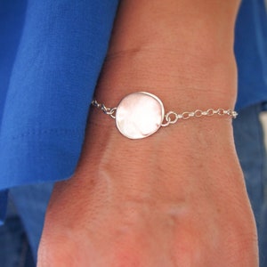 May include: A silver bracelet with a large, round, smooth charm. The charm is attached to a delicate silver chain.