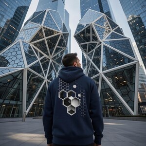 May include: Navy blue hoodie with a geometric design on the back. The design features a honeycomb pattern with black, white, and gray hexagonal shapes. The hoodie has a hood and is made of a soft material.