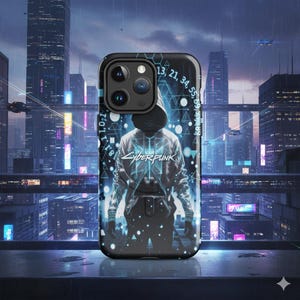 Op de afbeelding: Zwarte telefoonhoes met een futuristisch ontwerp. Het heeft een figuur met capuchon en het woord "CYBERPUNK" in het wit. De hoes heeft een zwarte cameramodule en een achtergrond van een stadsgezicht met neonlichten en vliegende voertuigen.