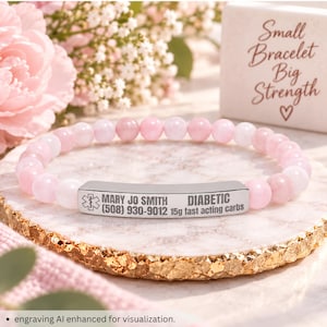May include: A medical alert bracelet featuring light pink and white beads and a silver-toned metal bar. The bar is engraved with a medical symbol, the name MARY JO SMITH, the phone number (508) 930-9012, the word DIABETIC, and 15g fast acting carbs.