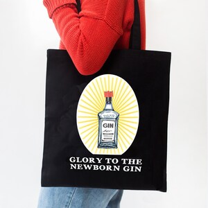 May include: Black tote bag with a white graphic of a bottle of gin with the text "Glory to the Newborn Gin".