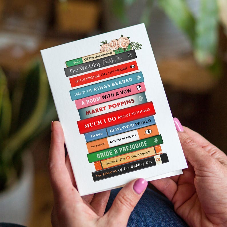 Pode incluir: Um cart&atilde;o branco com uma pilha de livros coloridos, incluindo "The Wedding Bells Jar" e "Bride & Prejudice". Detalhes florais no topo. O cart&atilde;o &eacute; segurado.