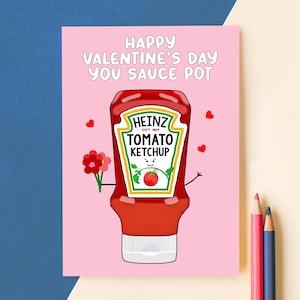 May include: A Valentine's Day card with a pink background features a cartoon ketchup bottle holding flowers. The card reads "HAPPY VALENTINE'S DAY YOU SAUCE POT" in white text. Small red hearts are scattered around the ketchup bottle.