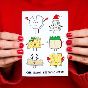 May include: A white card with a festive Christmas message, "CHRISTMAS FESTIVI-CHEESE!" and illustrations of various cheeses with faces and holiday attire. The cheeses include a brie with reindeer antlers, a cheddar with a holly sprig, a blue cheese with a Santa hat, a Swiss cheese with a green crown, and a cheddar with red mittens.