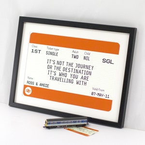 May include: A framed print of a vintage train ticket with the text "It's not the journey or the destination, it's who you are traveling with." The ticket is orange and white with black text. The name on the ticket is "Ross & Angie".