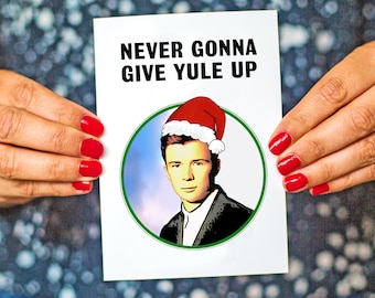 May include: A white card with the text "NEVER GONNA GIVE YULE UP" in black. A cartoon image of a man wearing a red Santa hat is in the center of the card.