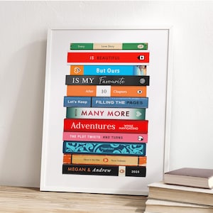 May include: A framed print showing a stack of book spines with titles such as "Every Love Story", "Is Beautiful", and "But Ours". The print also includes "Is My Favourite", "Adventures", and "Megan & Andrew 2025". The frame is white.