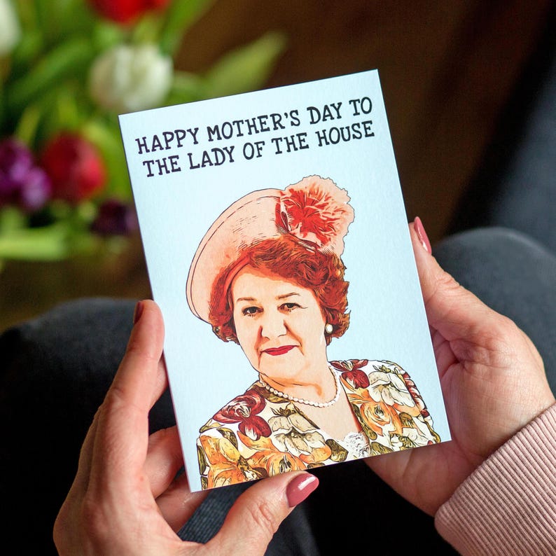 Puede incluir: Una tarjeta de felicitaci&oacute;n del D&iacute;a de la Madre con el texto "HAPPY MOTHER'S DAY TO THE LADY OF THE HOUSE." La tarjeta presenta un retrato de una mujer con sombrero y chaqueta floral. La tarjeta est&aacute; en manos de alguien.