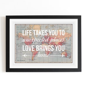 Op de afbeelding: Een ingelijst print met een vintage wereldkaart als achtergrond. De tekst "LIFE TAKES YOU TO unexpected places LOVE BRINGS YOU home" is in wit op de kaart gedrukt.