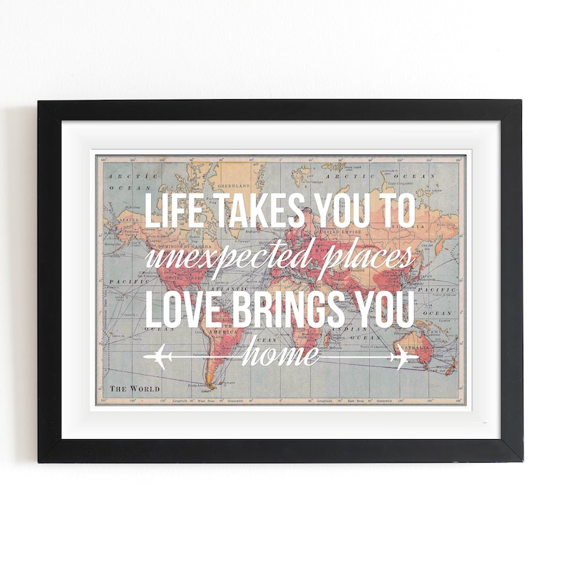 Op de afbeelding: Een ingelijst print met een vintage wereldkaart als achtergrond. De tekst "LIFE TAKES YOU TO unexpected places LOVE BRINGS YOU home" is in wit op de kaart gedrukt.