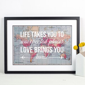 Op de afbeelding: Een ingelijst afdruk met een vintage wereldkaart en de tekst "LIFE TAKES YOU TO unexpected places LOVE BRINGS YOU home".