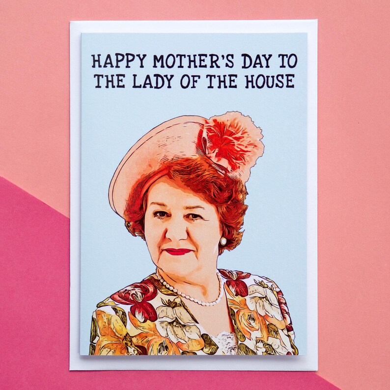 Puede incluir: Tarjeta de felicitaci&oacute;n del D&iacute;a de la Madre con el retrato de una mujer con sombrero y chaqueta floral. El texto "HAPPY MOTHER'S DAY TO THE LADY OF THE HOUSE" est&aacute; impreso en negro. La tarjeta est&aacute; sobre un fondo azul claro, sobre un fondo rosa.