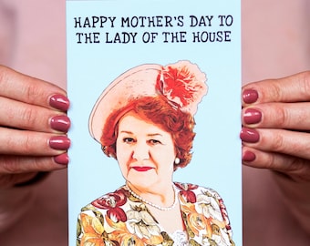Puede incluir: Tarjeta azul claro del Día de la Madre con el texto "HAPPY MOTHER'S DAY TO THE LADY OF THE HOUSE". La tarjeta presenta un retrato de una mujer con sombrero y top con estampado floral.