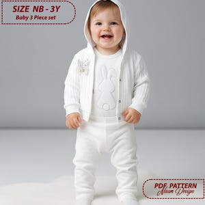 May include: A baby wearing a white three-piece set. The set includes a hooded cardigan, a long-sleeved shirt with a bunny design, and matching pants. The text "SIZE NB - 3Y Baby 3 Piece set" is visible. The baby is standing on a white surface.