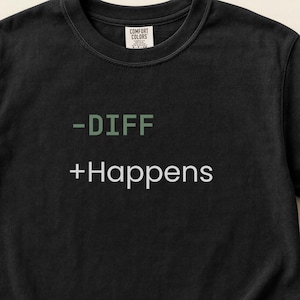 May include: Black t-shirt with the text "-DIFF +Happens" in green and white. The shirt is made of a soft material and has a classic crew neck design. The Comfort Colors brand label is visible at the top.