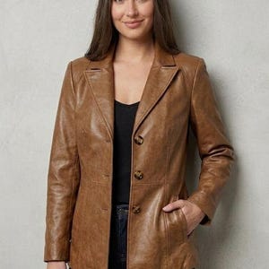 Op de afbeelding: Een lichtbruine leren blazer met een ingekeepte revers, lange mouwen en een sluiting met drie knopen aan de voorzijde. De jas heeft twee zijzakken en verticale naaddetails aan de voorzijde, wat zorgt voor een gestructureerde pasvorm.