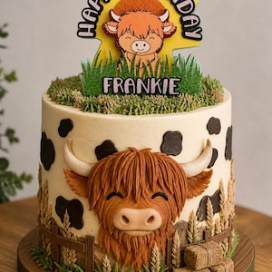 Può includere: Una torta di compleanno decorata a tema mucca delle Highlands. La torta ha una base color crema con macchie nere di mucca e un volto di mucca dettagliato. La torta è sormontata da un topper "Happy Birthday Frankie" ed erba decorativa.