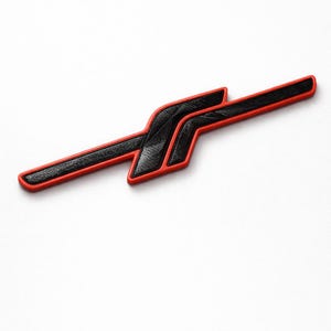 May include: A black and red emblem with a unique design. The emblem has a textured black center with a red border. The shape is a stylized, angular design, possibly for automotive or decorative use.